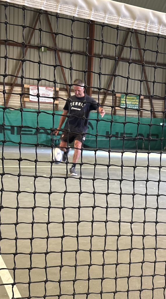 Olivier Miranda kicks a rugby ball on an indoor tennis court, seen through the net